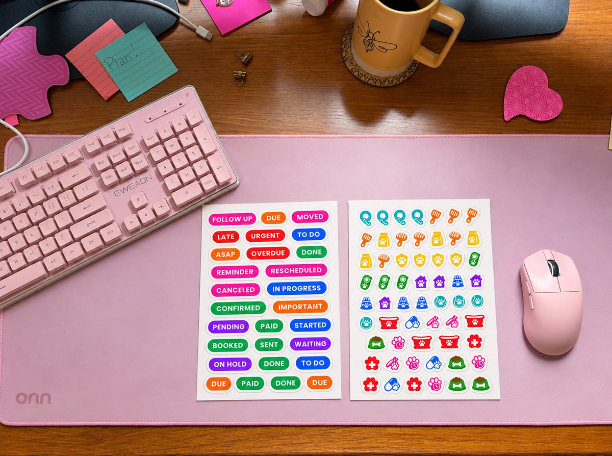 Two kiss-cut planner sticker sheets on a pink desk mat: a status label sheet reading Follow Up, Due, Moved, Canceled, In Progress, Paid, Sent and Waiting, beside a pets icon sheet of paws, bowls and grooming brushes