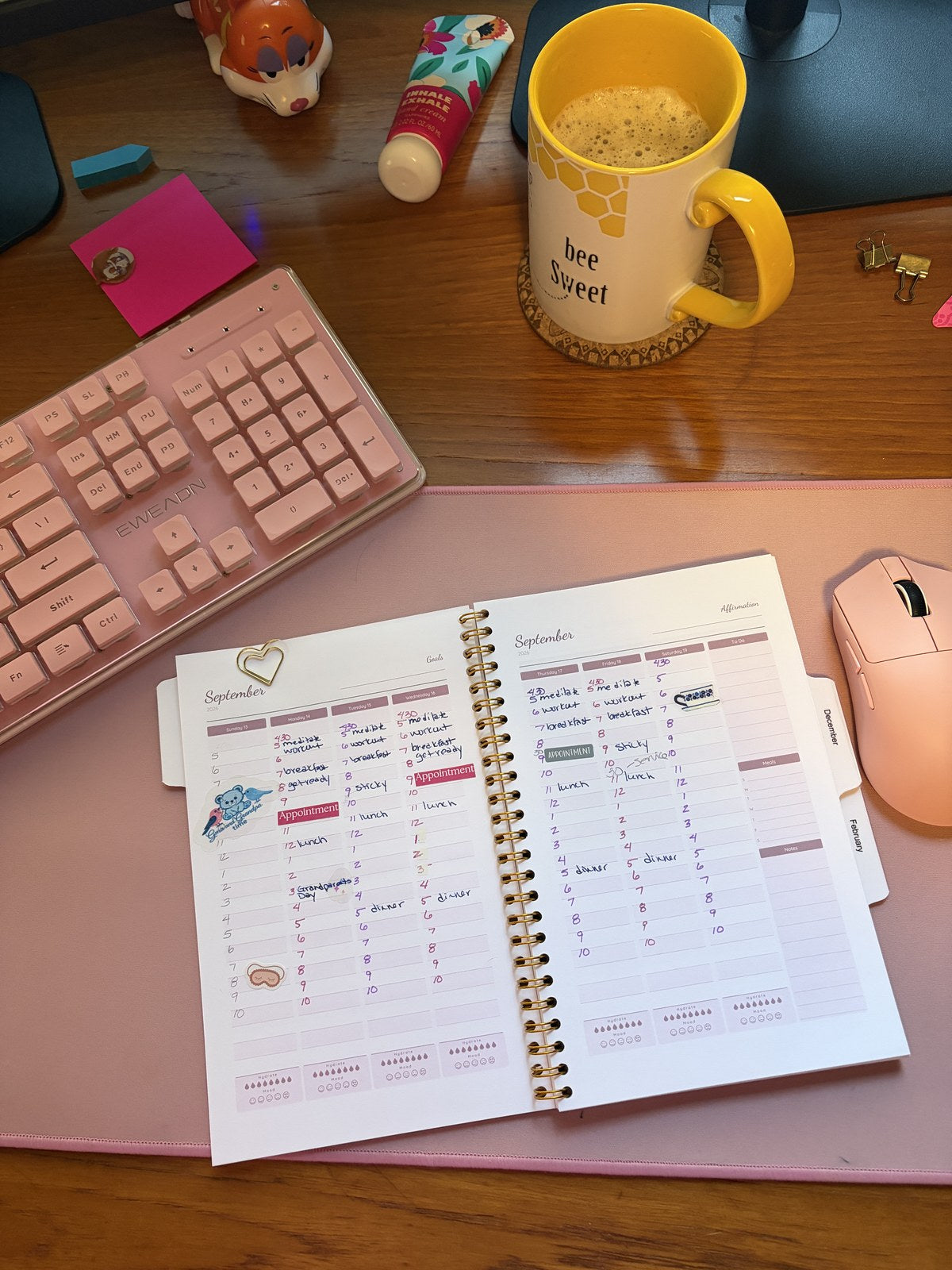 Open weekly planner spread on a pink desk mat with a handwritten morning routine, Appointment labels and a yellow bee mug